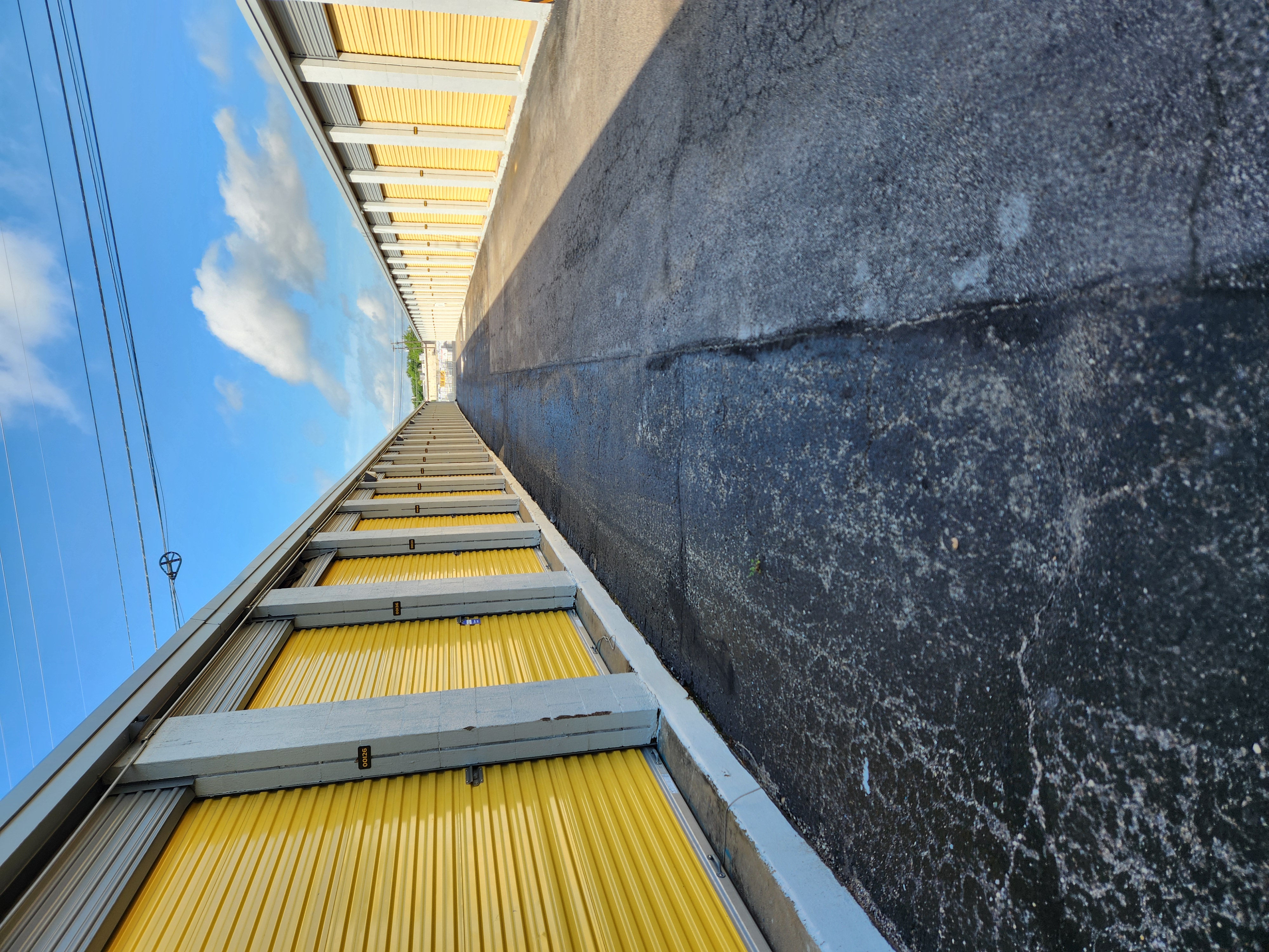 Row of secure yellow drive-up storage units at Round Rock Secure Storage near Hutto, TX, under a bright blue sky.